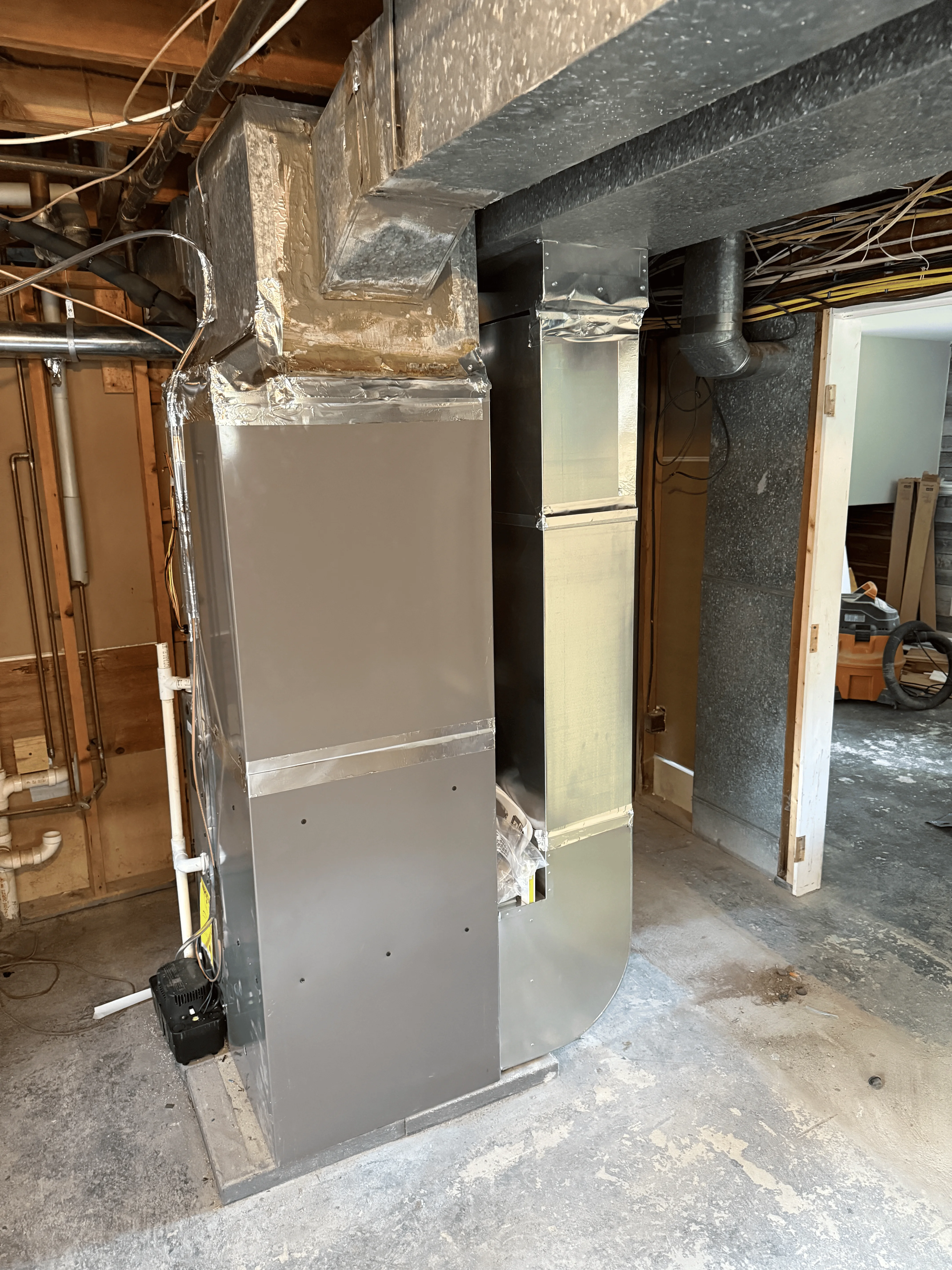 New gray furnace unit installed in basement with black ductwork and foil-sealed connections