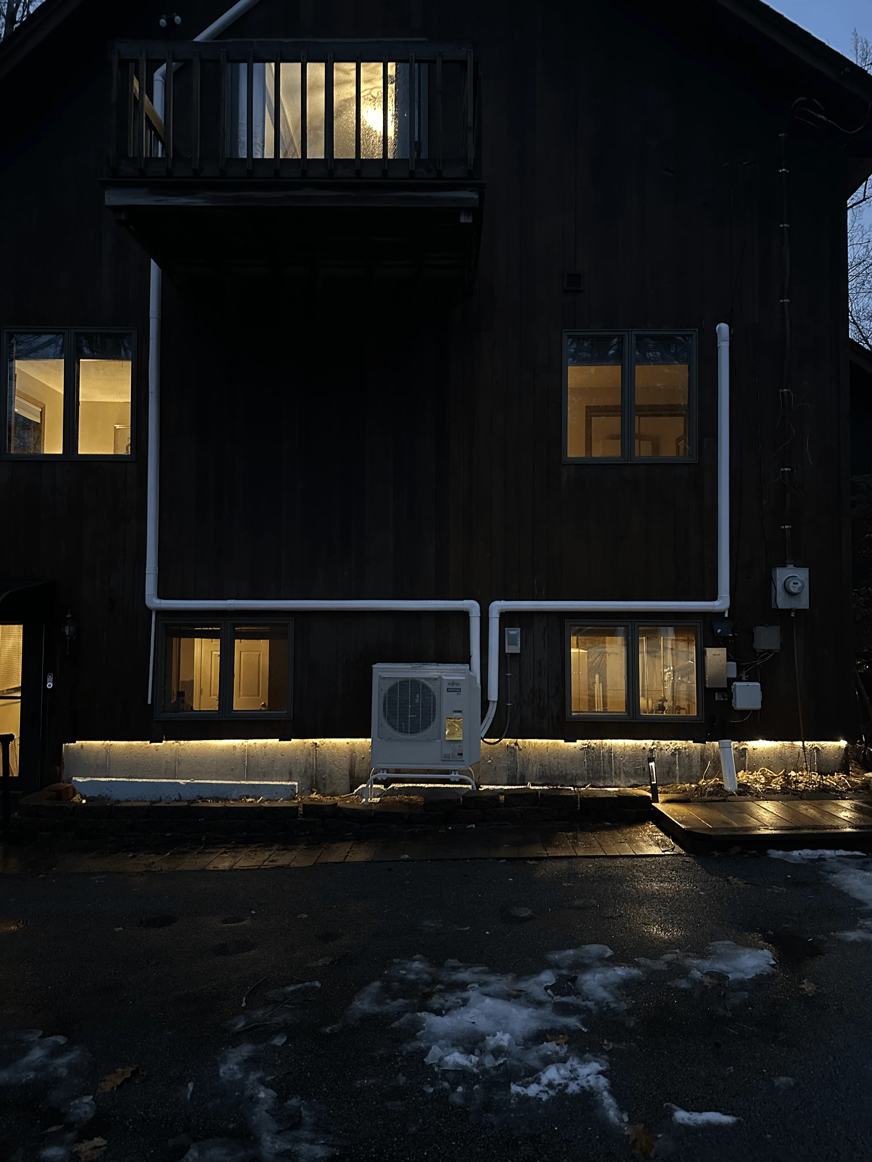 White mini-split HVAC outdoor unit installed on black residential building foundation at night