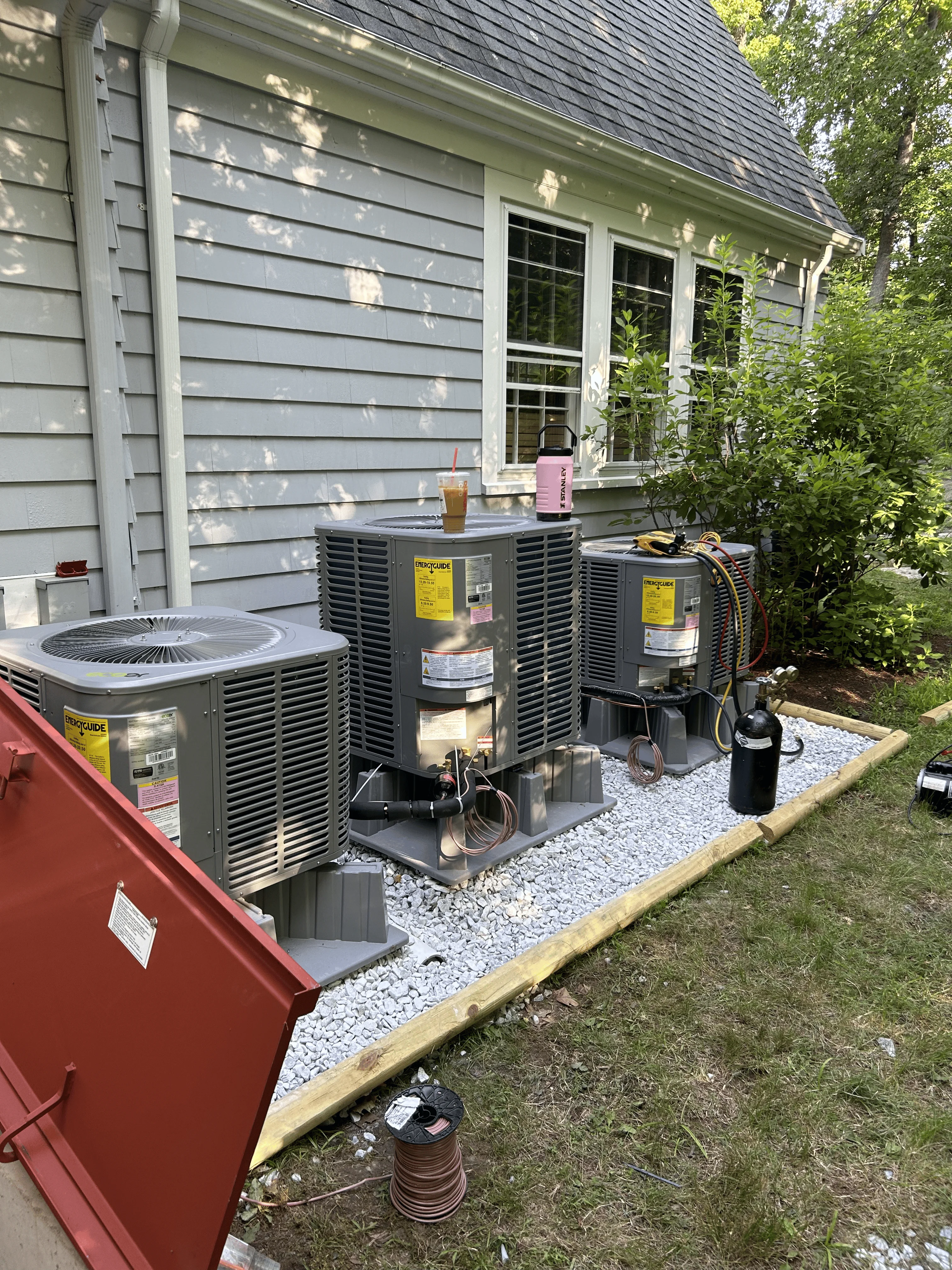 Two gray HVAC condensing units installed on gravel pad beside residential home with white trim