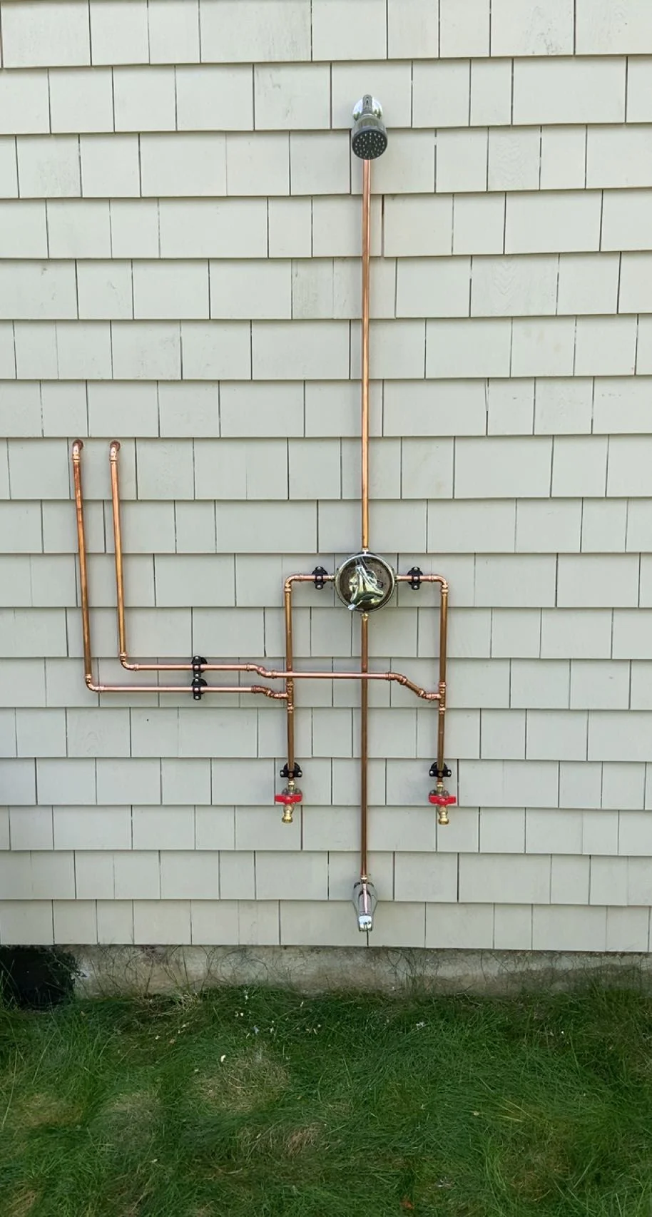 Copper outdoor shower plumbing system mounted on white cedar shake siding with rainfall head and dual valves