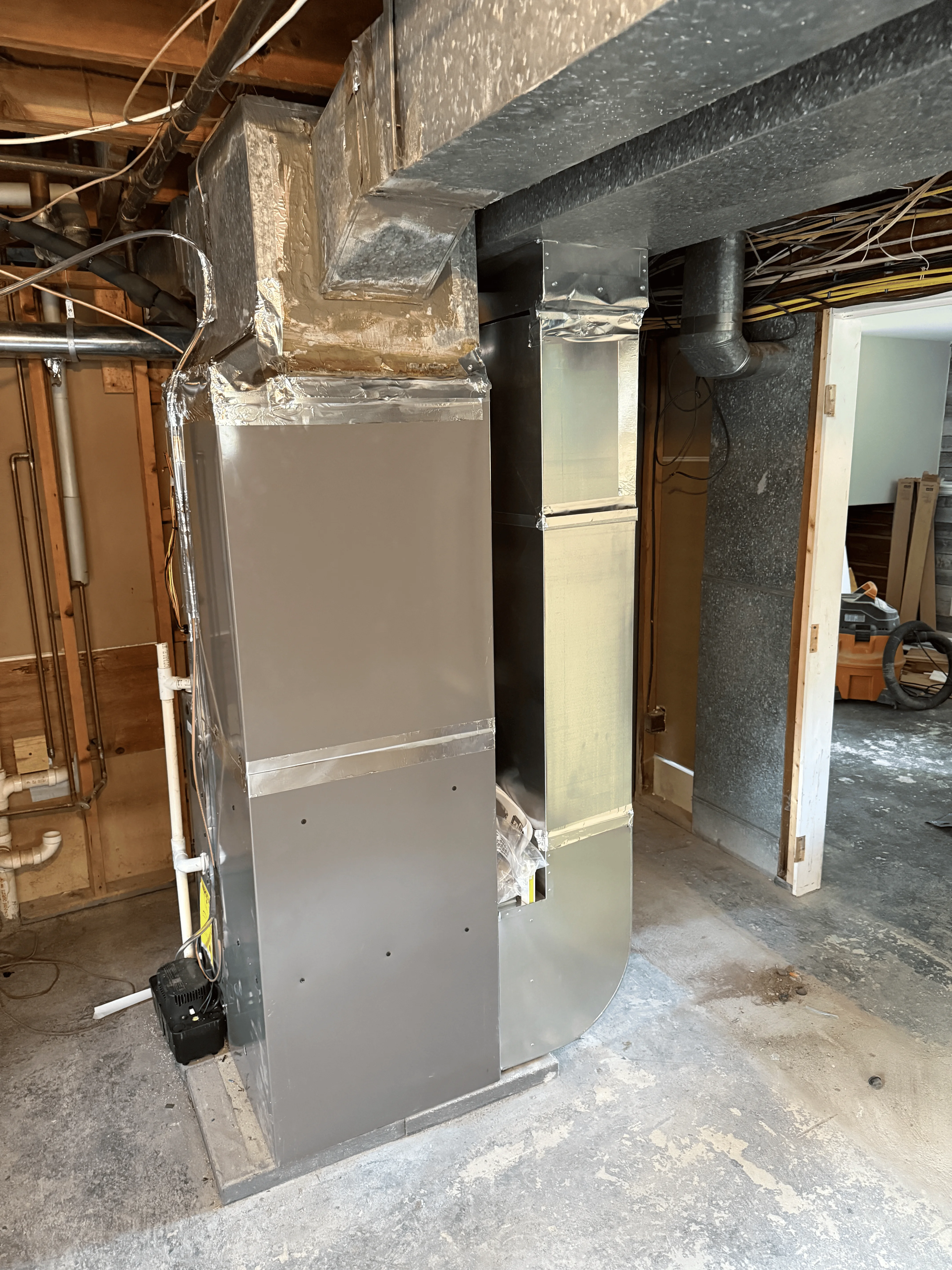 New gray furnace unit installed in basement with black ductwork and insulation wrap