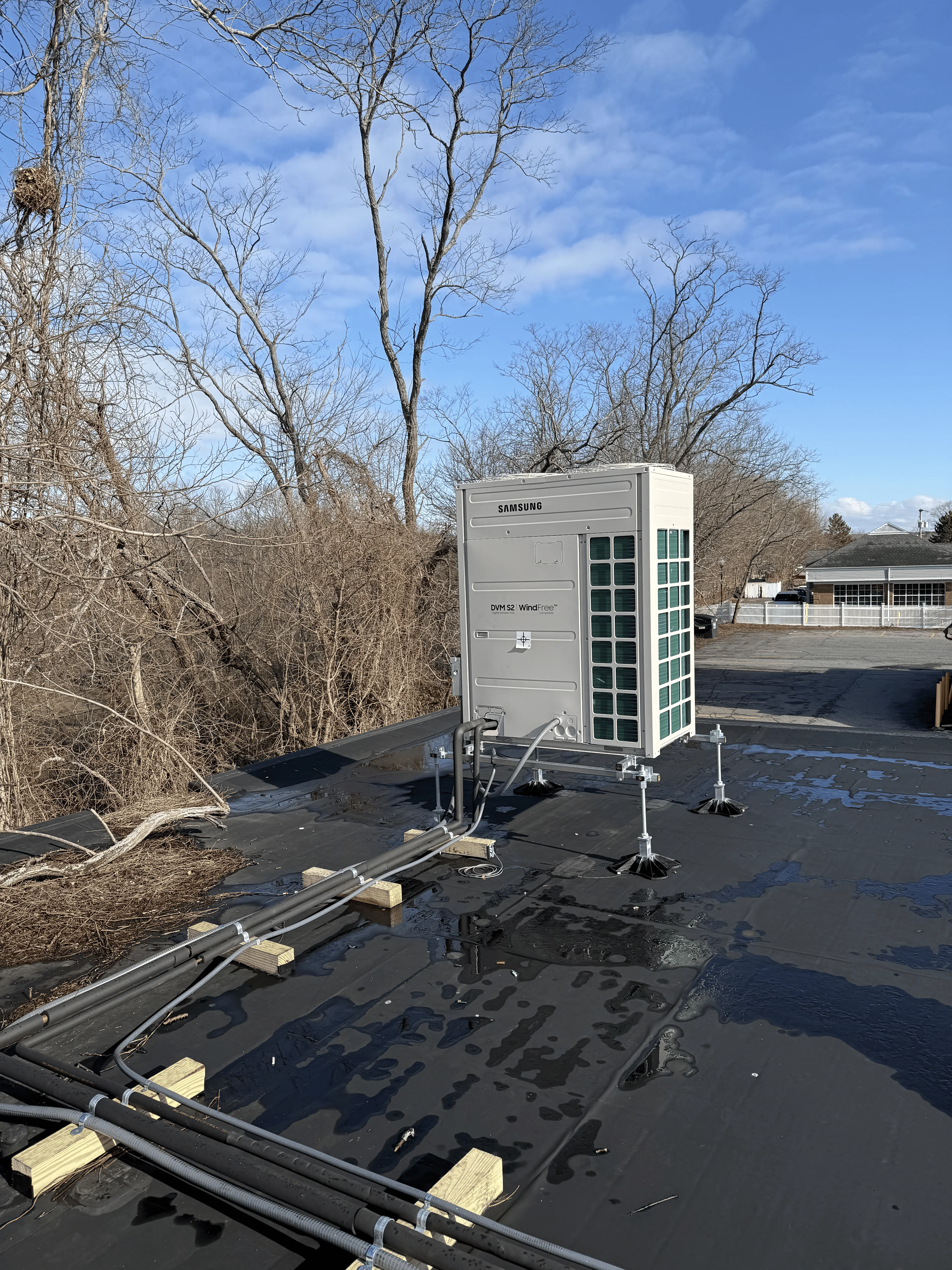 Samsung commercial heat pump unit installed on flat roof with metal support frame and wooden blocking