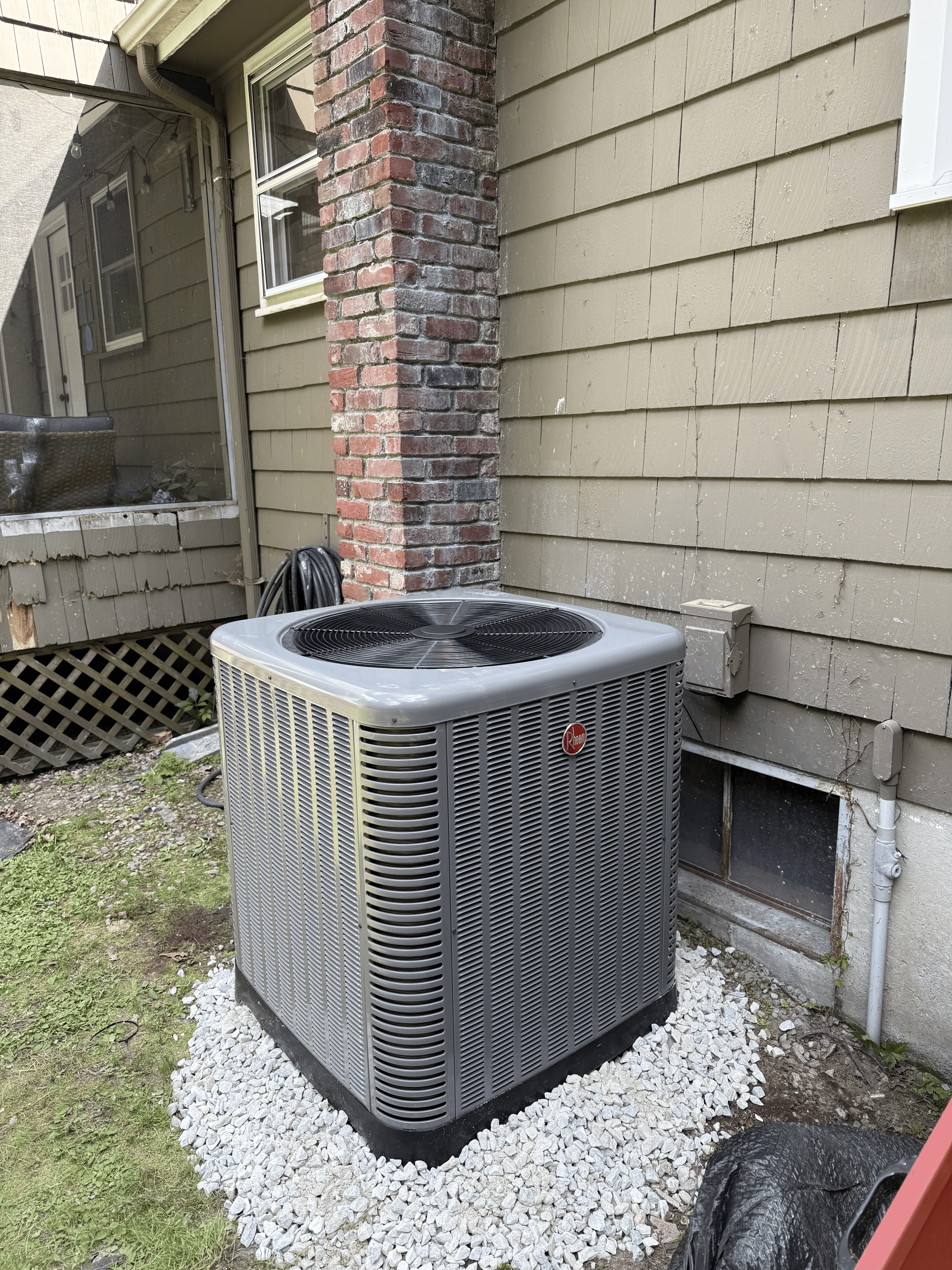 New AC condenser unit installed on gravel pad next to brick chimney